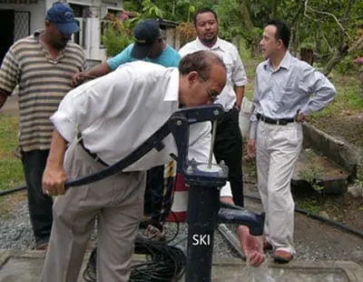 Officials testing an SKI shallow well hand pump with water flowing from the spout