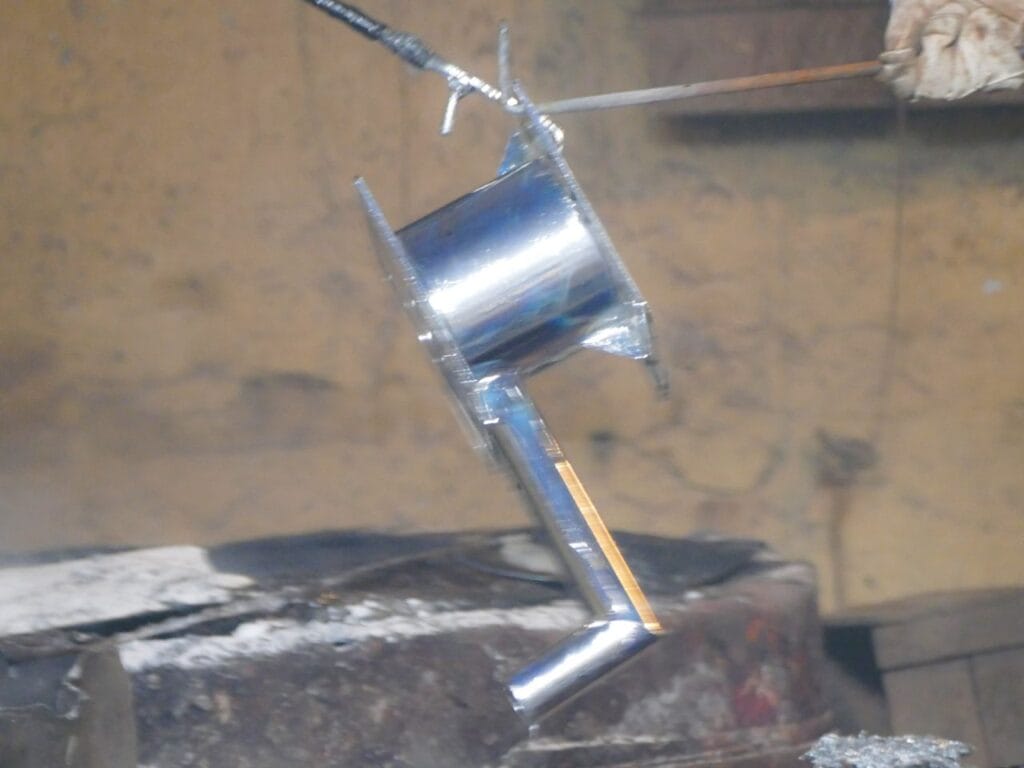 Hand pump component being pulled from the molten zinc bath, freshly coated during hot-dip galvanizing