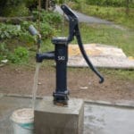 SKI shallow well hand pump installed on a concrete platform, running water into a bucket