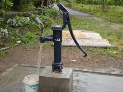 SKI shallow well hand pump installed on a concrete platform, running water into a bucket