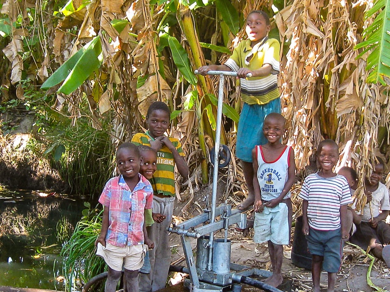 Children operating an SKI metal treadle pump to draw water from a stream in a rural African community