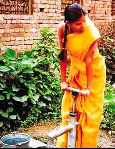 Woman operating a Tara hand pump to draw water into a bucket in a rural setting